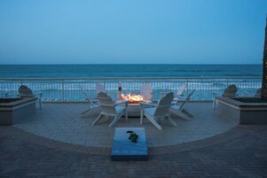 Una terraza con sillas Adirondack, un pozo de fuego y vista al océano.