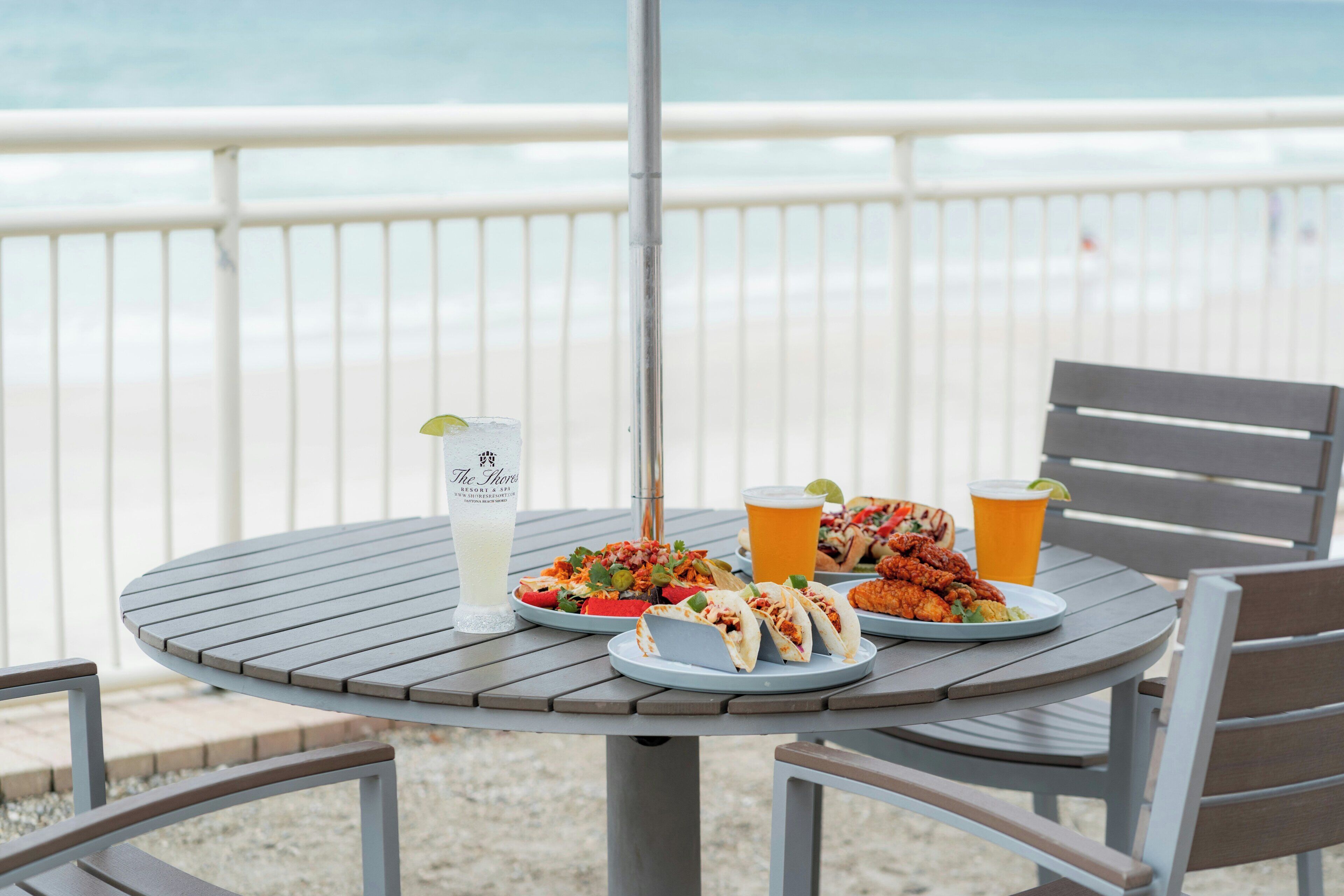 Ein Tisch mit Getränken, Tacos und einer Speisenplatte auf einem Balkon mit Blick auf den Strand.