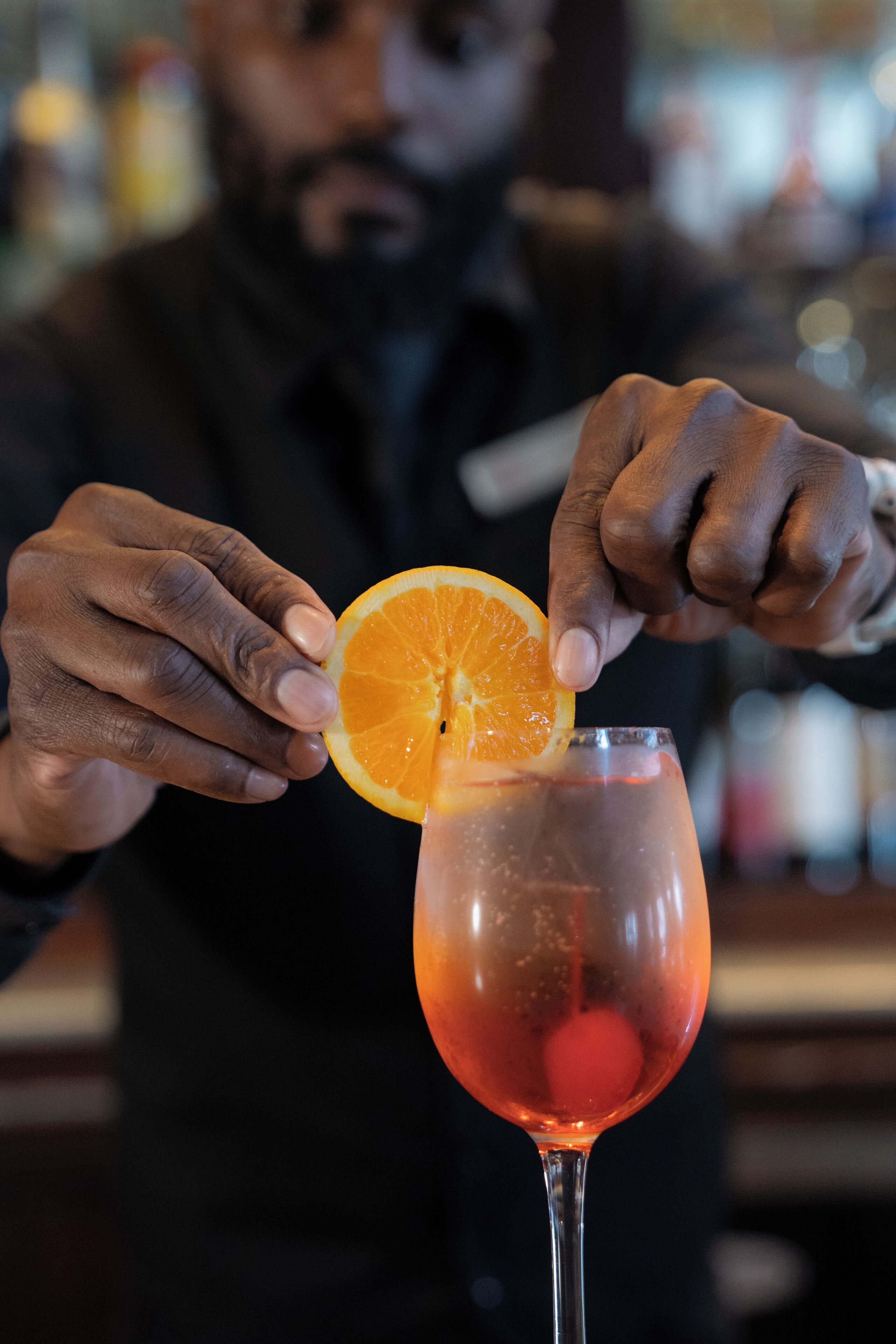A person placing an orange slice on a drink in a glass.
