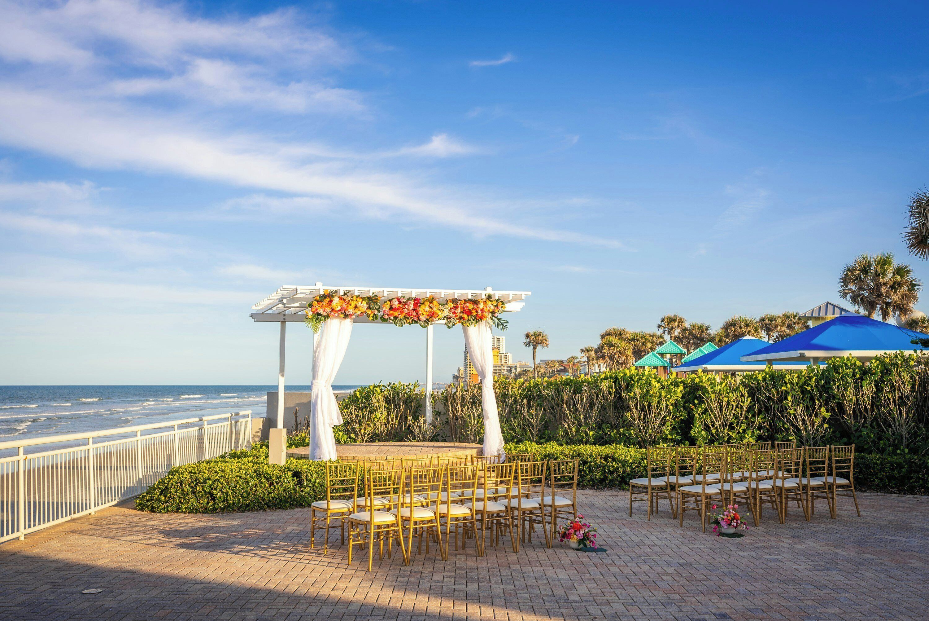 An outdoor wedding setup with a white arch and floral decorations, overlooking the ocean.