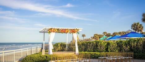An outdoor wedding setup with a white arch and floral decorations, overlooking the ocean.