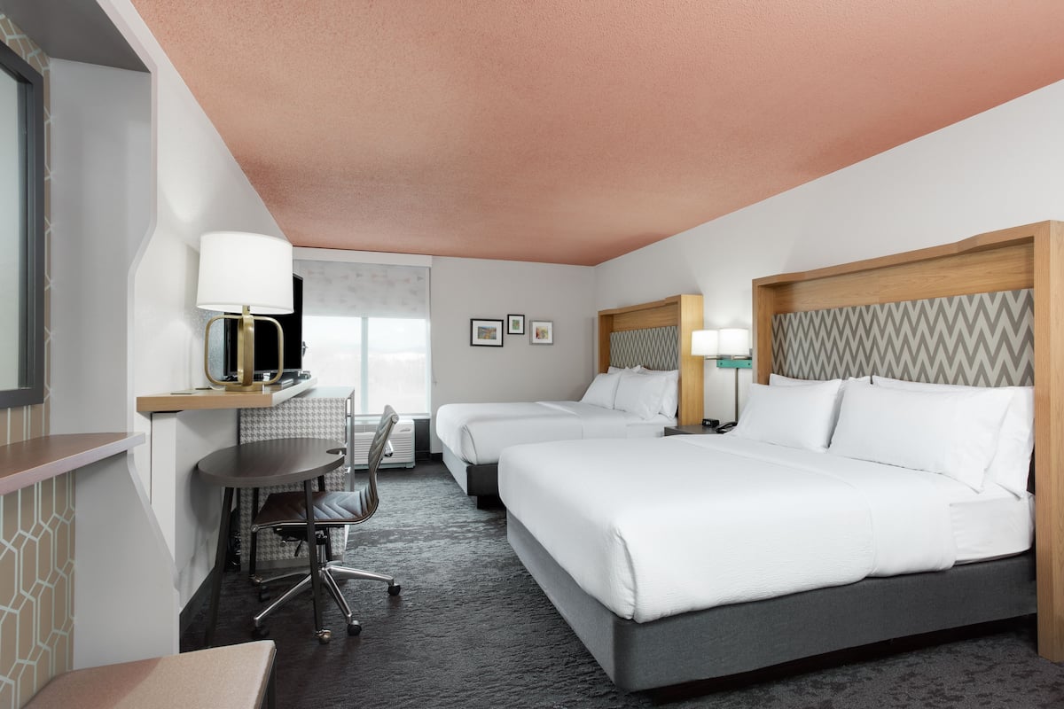 A hotel room with two beds, a desk with a chair, a small table, and a mirror.