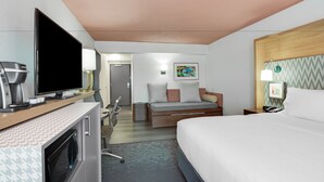 Ein Hotelzimmer mit Bett, Fernseher, Schreibtisch mit Kaffeemaschine, Stuhl und einer kleinen Küchenzeile.