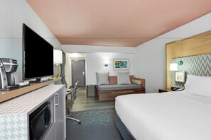 Une chambre d’hôtel comprenant un lit, une télévision, un bureau avec une machine à café, une chaise et une petite kitchenette.