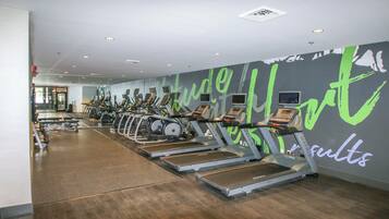Une salle de sport avec plusieurs tapis de course alignés le long d’un mur, et des messages motivants affichés.