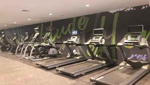 A gym with multiple treadmills and stationary bikes, a wall with motivational text, and a digital screen displaying workout content.