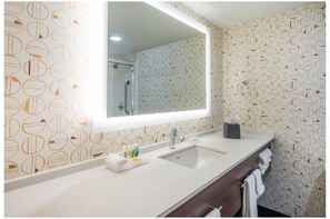 Une salle de bain avec un grand miroir, un lavabo et un meuble-lavabo doté d’un porte-serviettes.