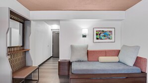 Ein modernes Hotelzimmer mit einer Holzbank, einem Sofa mit Kissen, einer Wandleuchte und einem farbenfrohen abstrakten Gemälde.