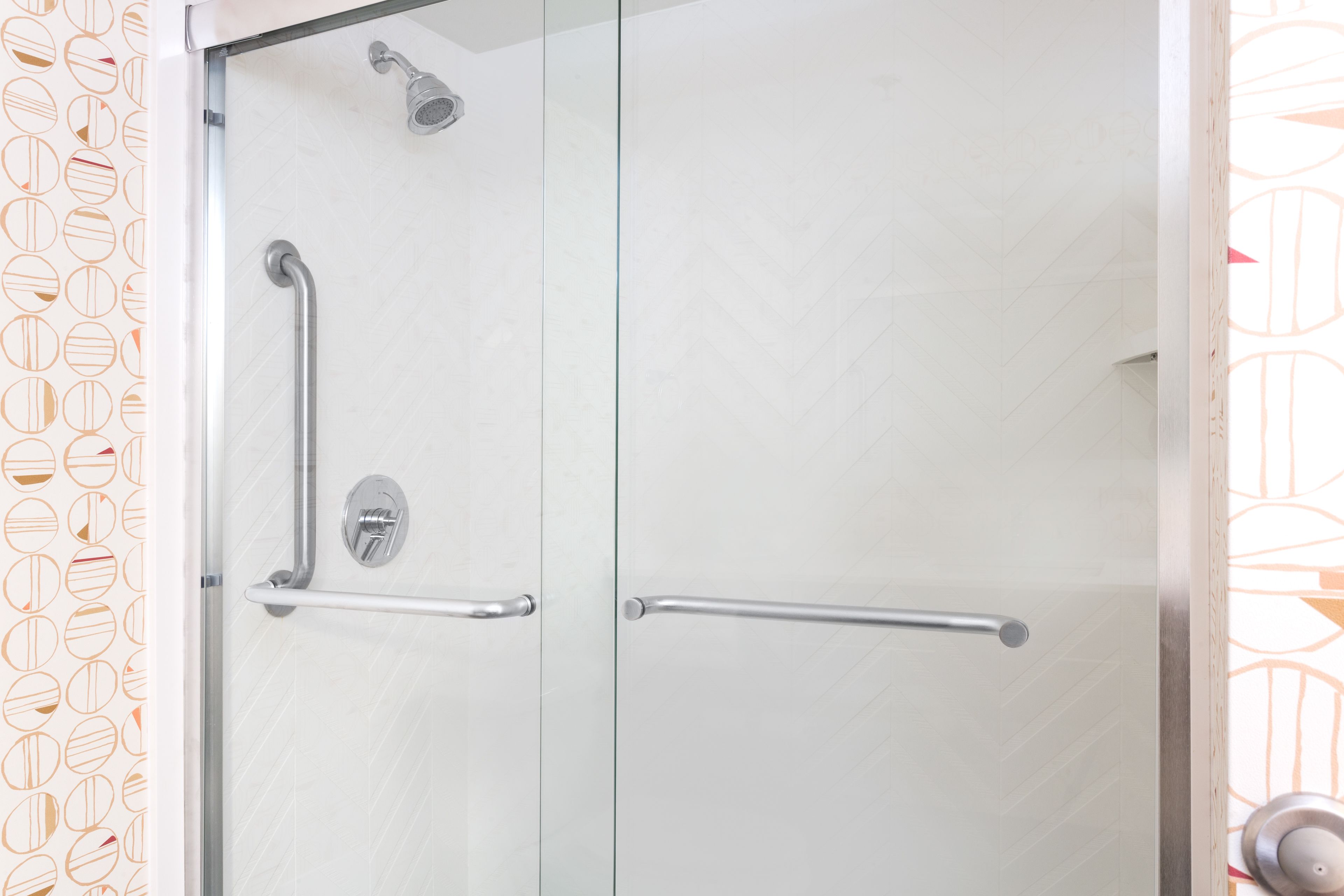 A shower with a glass door, a handrail, and a showerhead.