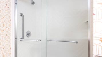 A shower with a glass door, a handrail, and a showerhead.