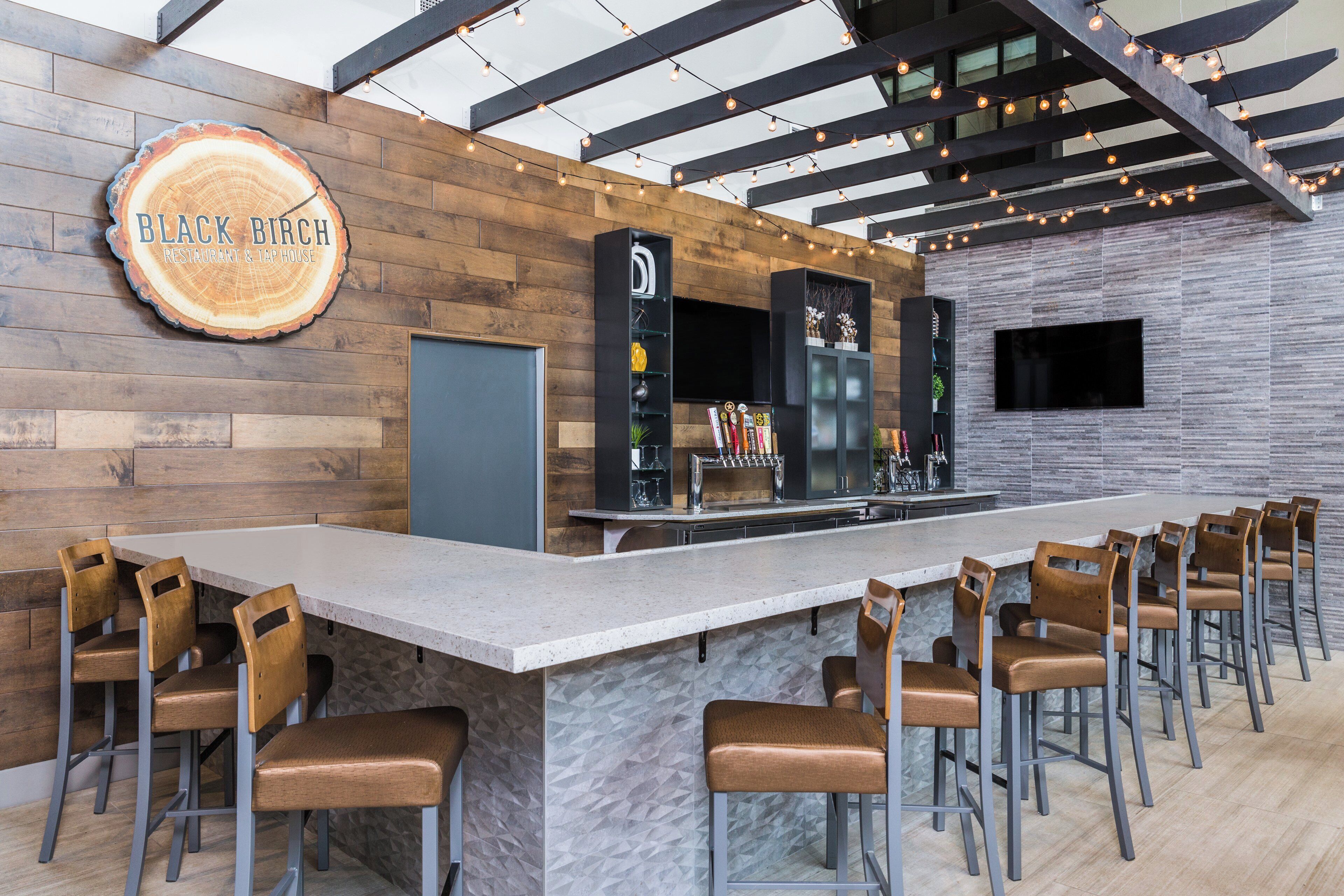 A bar area with a long counter, multiple stools, and a sign that reads 'BLACK BIRCH RESTAURANT & TAP HOUSE'.