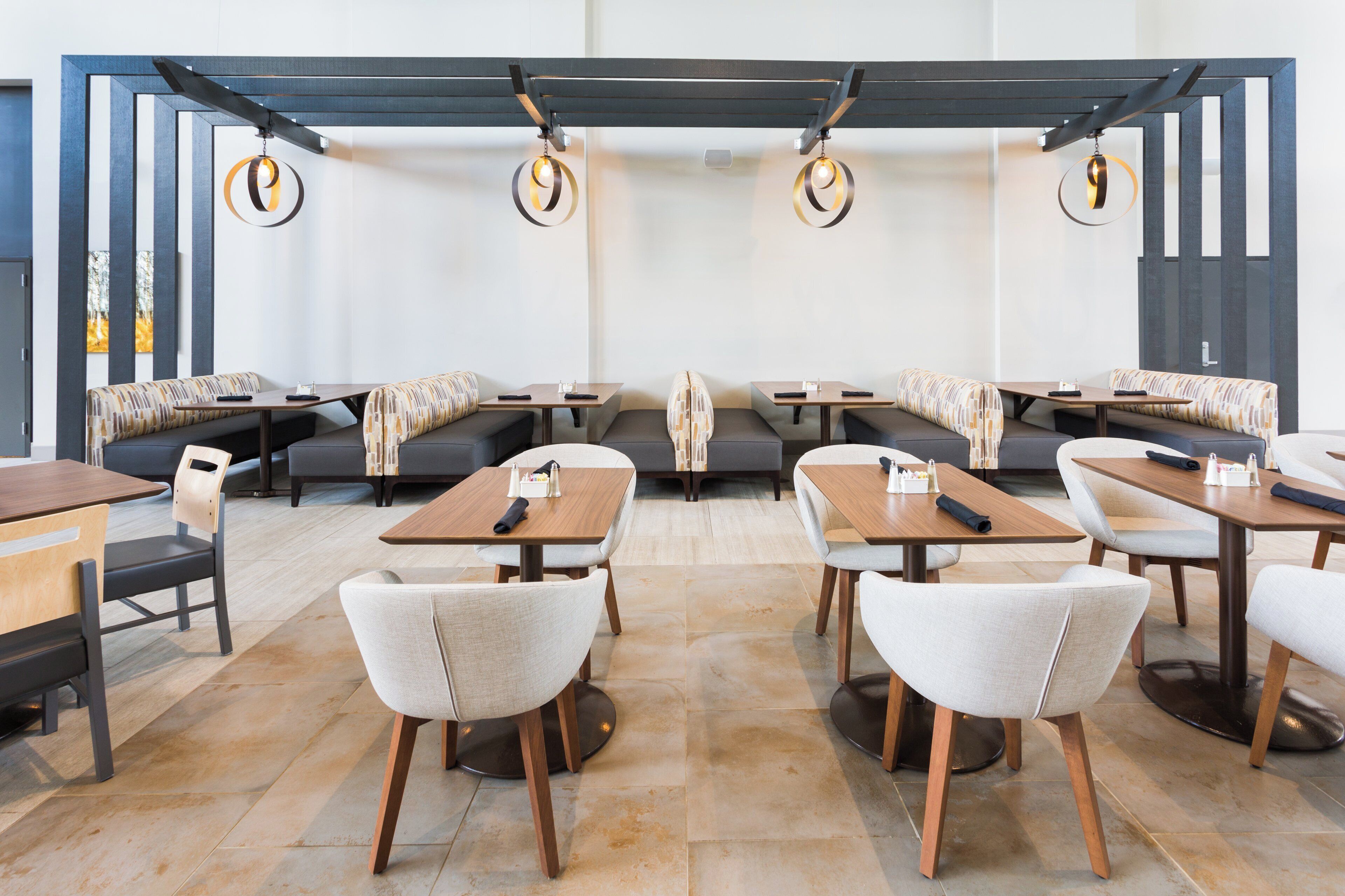 A modern restaurant with booths and tables, wooden flooring, and pendant lighting.