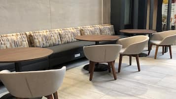 Un espacio moderno para sentarse con sofá y mesas redondas, ideal para comer o conversar.