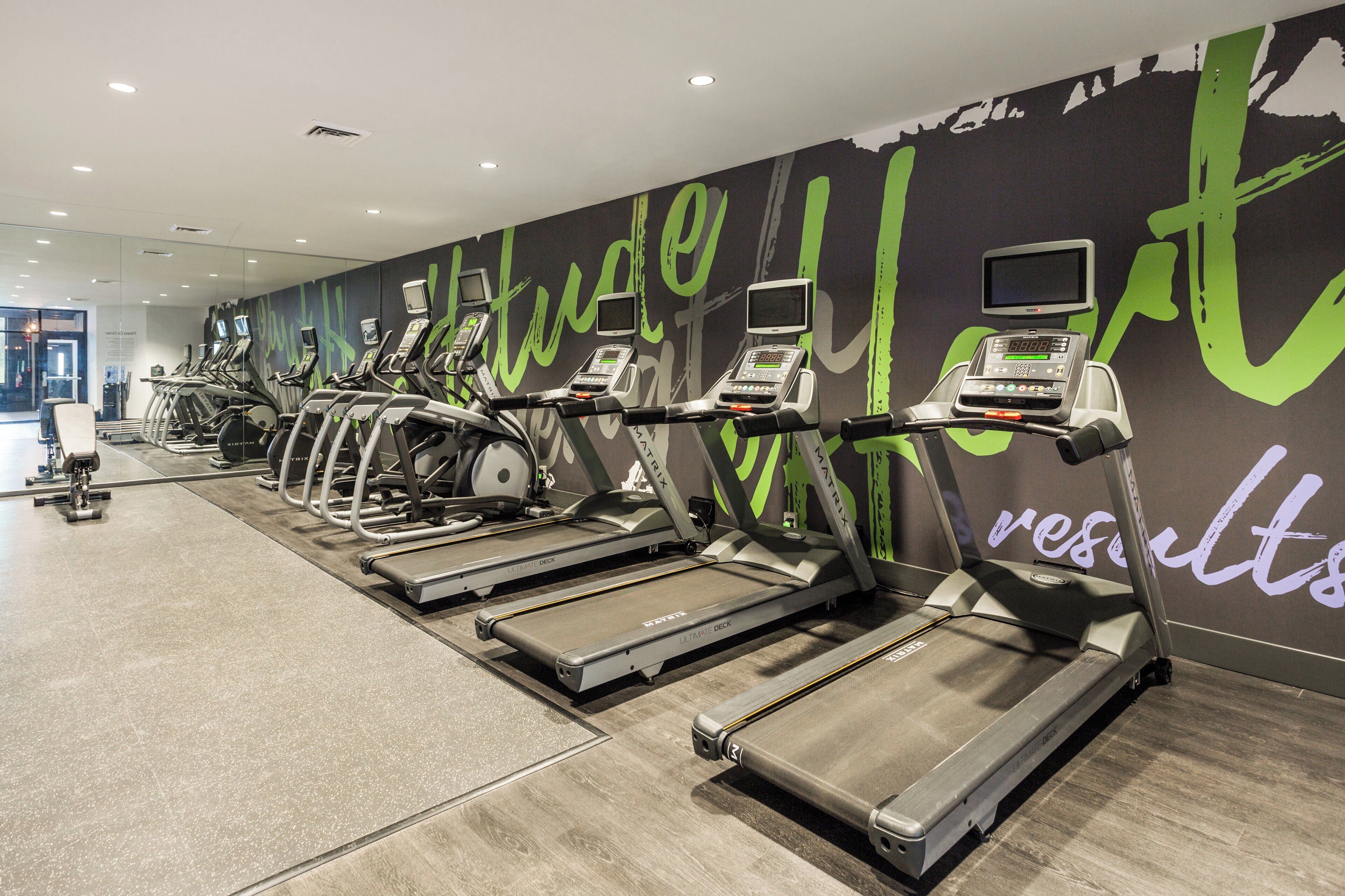 A gym with treadmills and stationary bikes, a wall with motivational text, and a visible exit door.