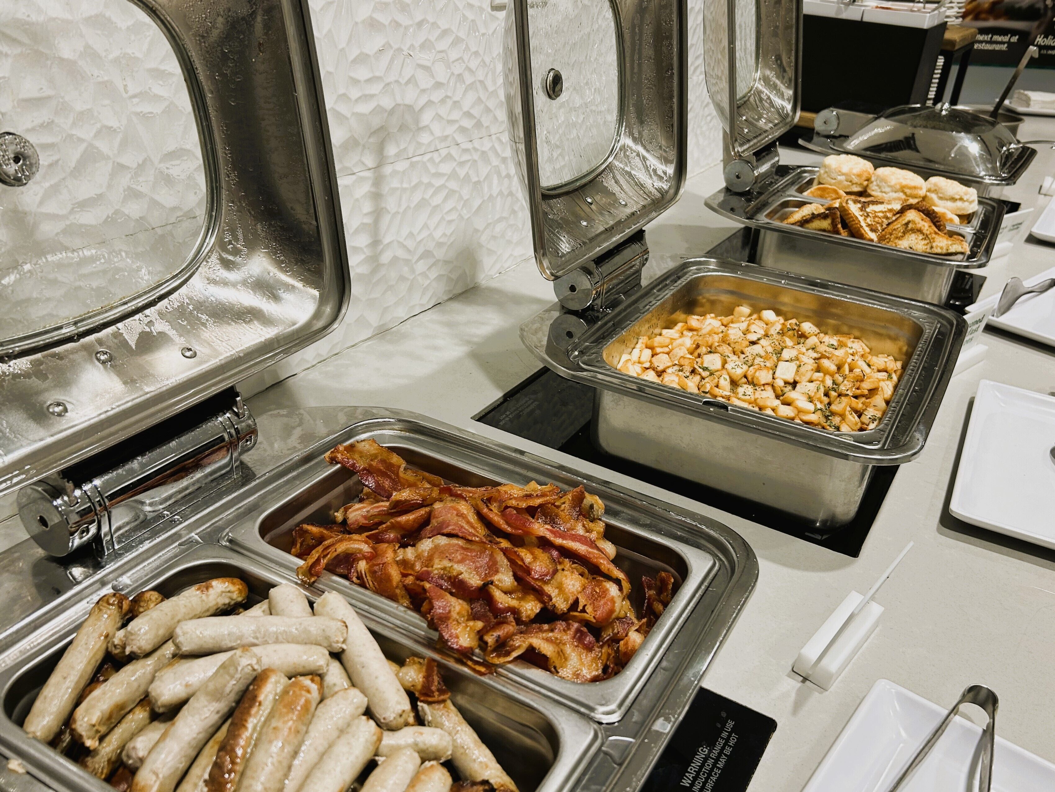 Un bufé con diversas opciones de comida, incluyendo salchichas, tocino y macarrones.