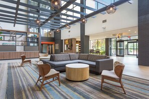 A spacious lobby with a sectional sofa, round coffee table, and wooden chairs. - Holiday Inn Roanoke Airport – Conference CTR by IHG (Roanoke)