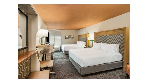 Une chambre d’hôtel avec deux lits, un bureau avec une chaise, un grand miroir et une moquette à motifs.