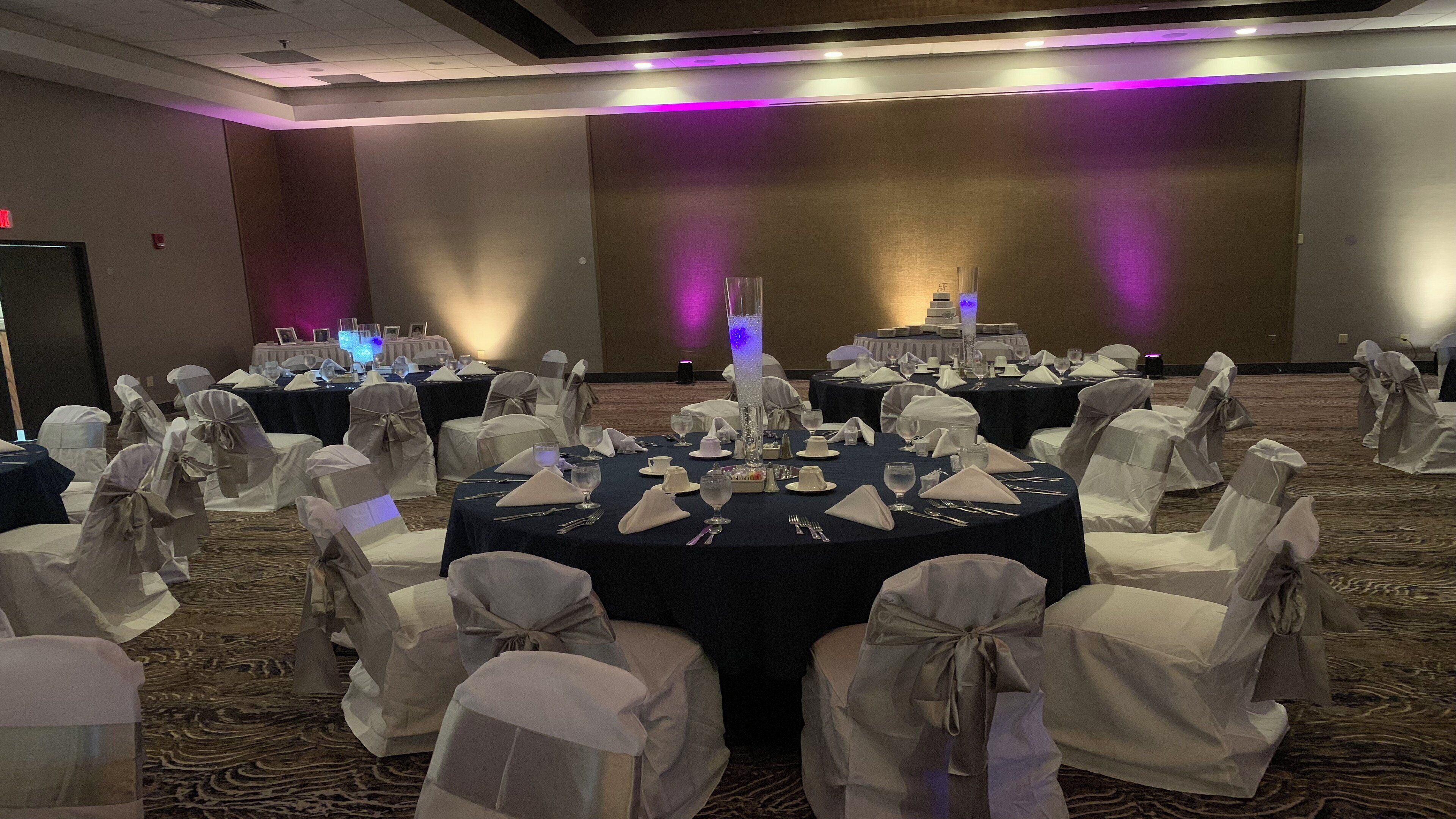A banquet hall with round tables set for dining, chairs with white covers, and a central decorative pillar.