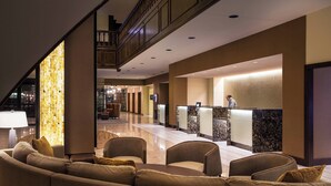 A modern hotel lobby with a reception desk, seating area, and a staircase.