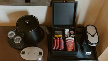 A hotel room with a black tray table, a tea set, a kettle, and a power outlet.