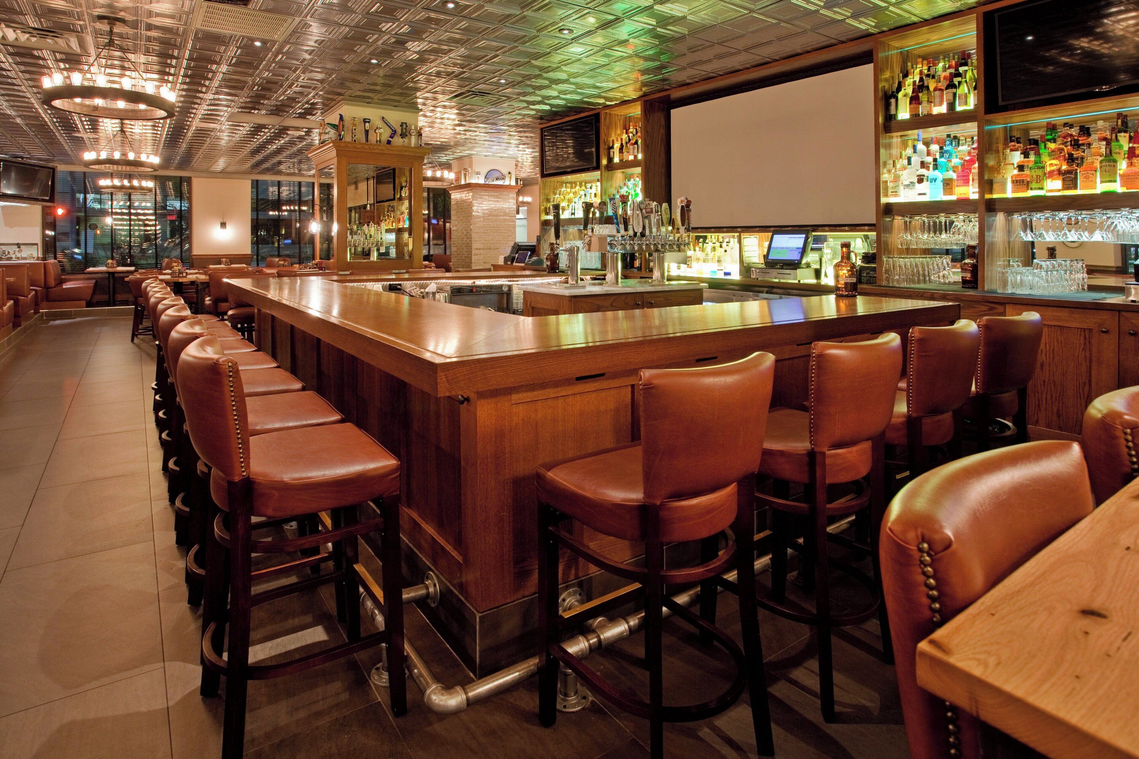 A bar area with wooden bar stools, a bar counter, and a variety of liquor bottles and glasses.