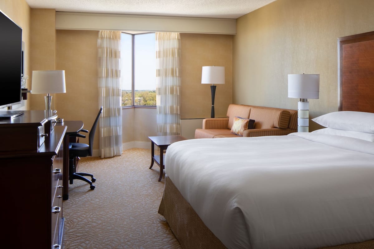 A hotel room with a large bed, a desk with a chair, a sofa, two lamps, and a TV.