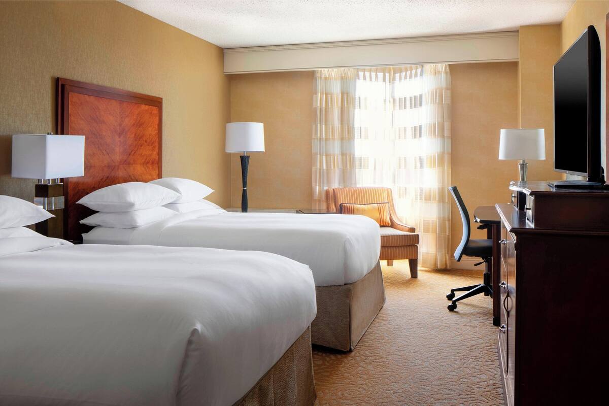 A hotel room with two beds, a desk, a chair, and a television.