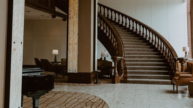 A grand lobby with a curved staircase, a grand piano, and a patterned carpet.