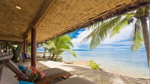 A beachside lounge with a thatched roof, lounge chairs, and a view of the ocean.