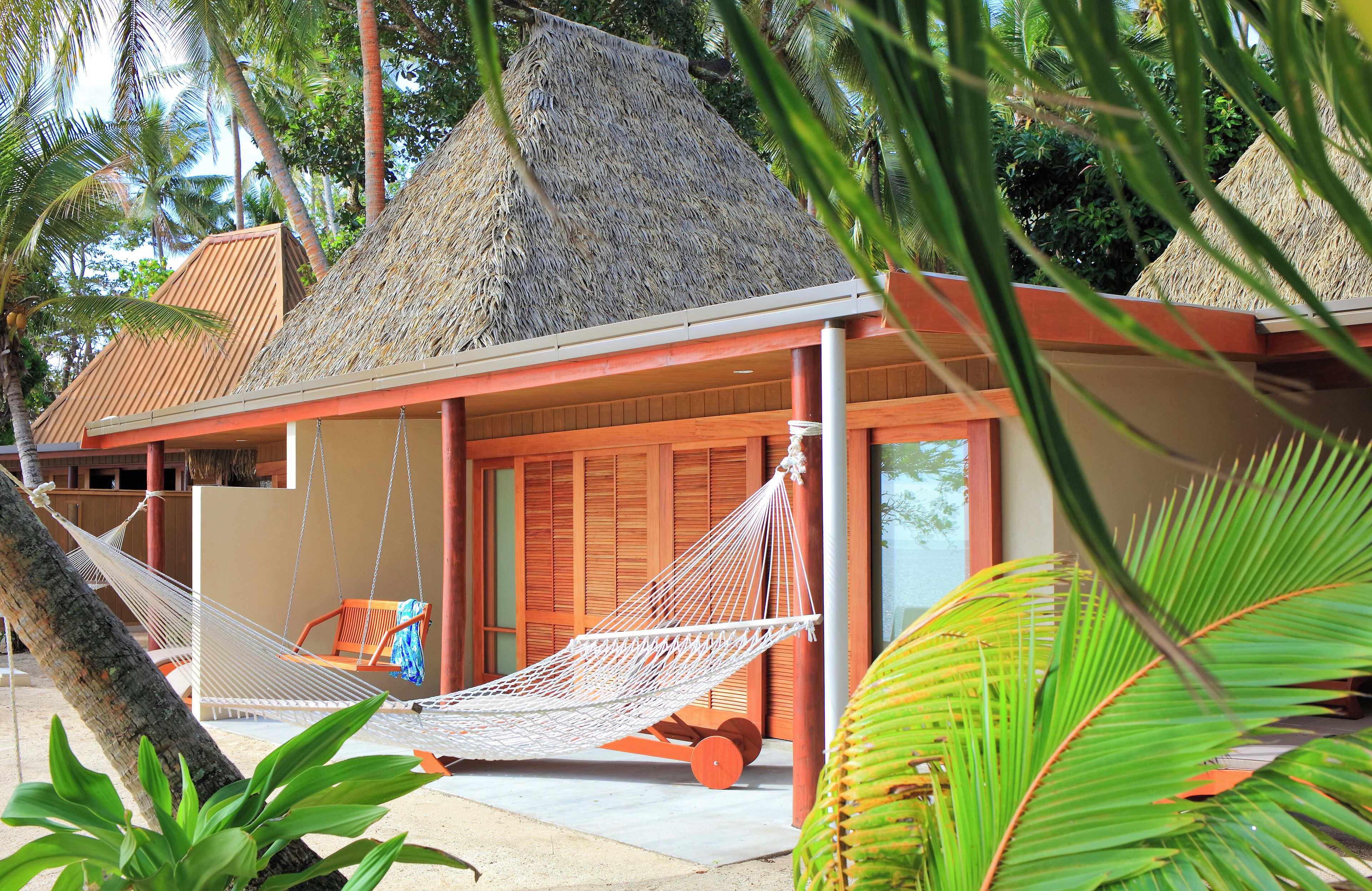 Un resort con edificios de techo de paja, una hamaca y exuberante vegetación tropical.