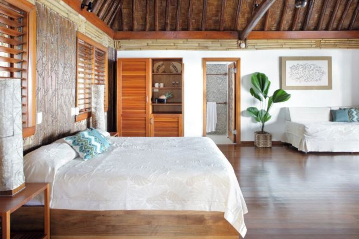 A bedroom with a wooden bed, a wardrobe, a bedside table, and a large window with wooden shutters.