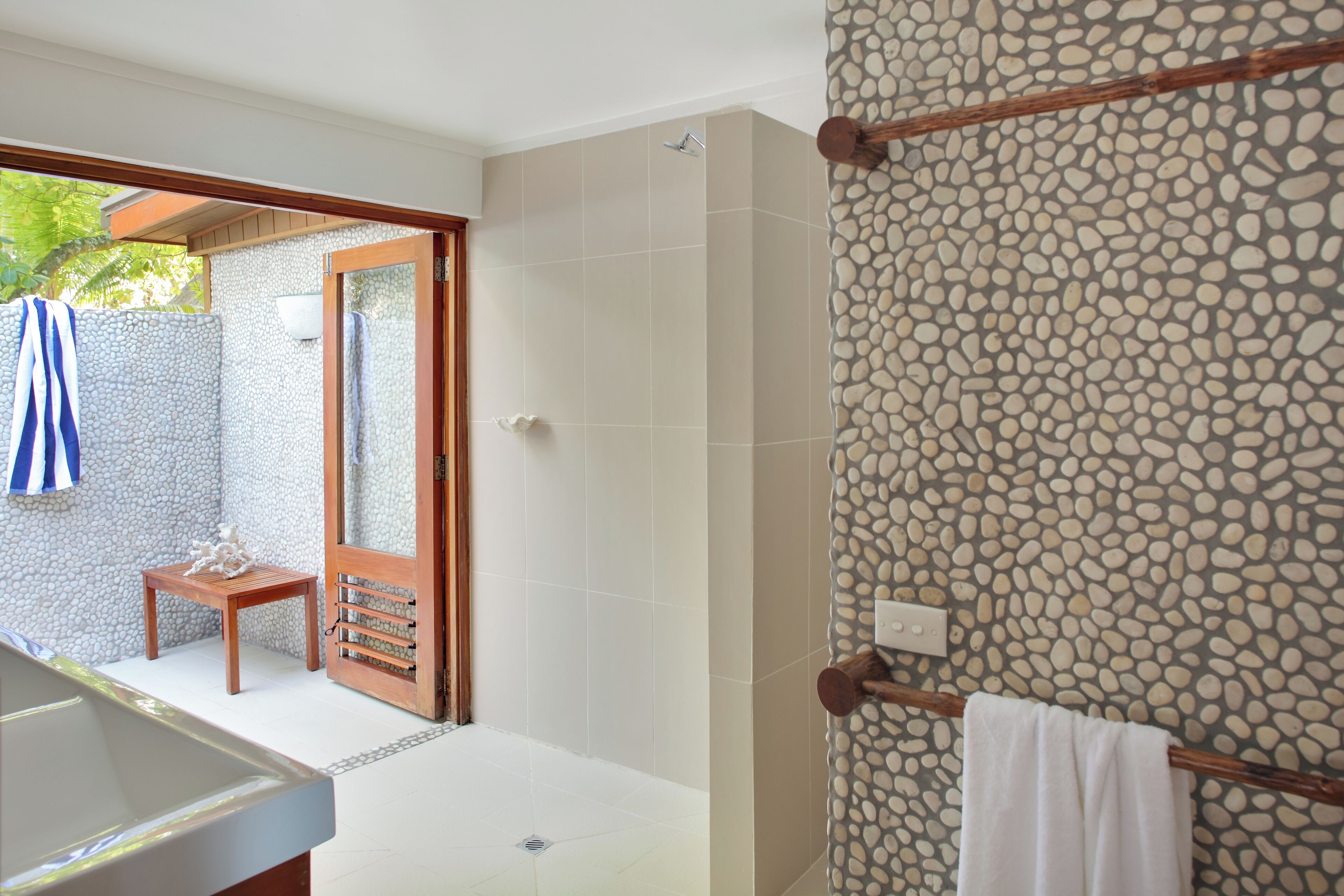 Une salle de bain avec une baignoire, une douche et un mur recouvert de carreaux formant un motif de galets.