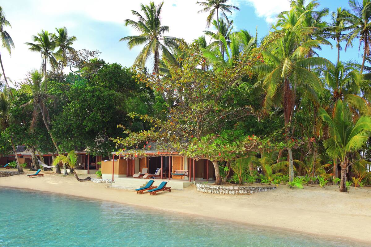 Un complexe hôtelier situé en bord de mer, avec une eau d’un bleu cristallin, des palmiers et des chaises longues.