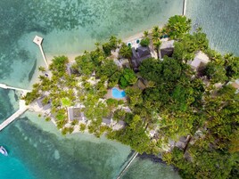 Vista aérea de un resort tropical con piscina, palmeras y un muelle.