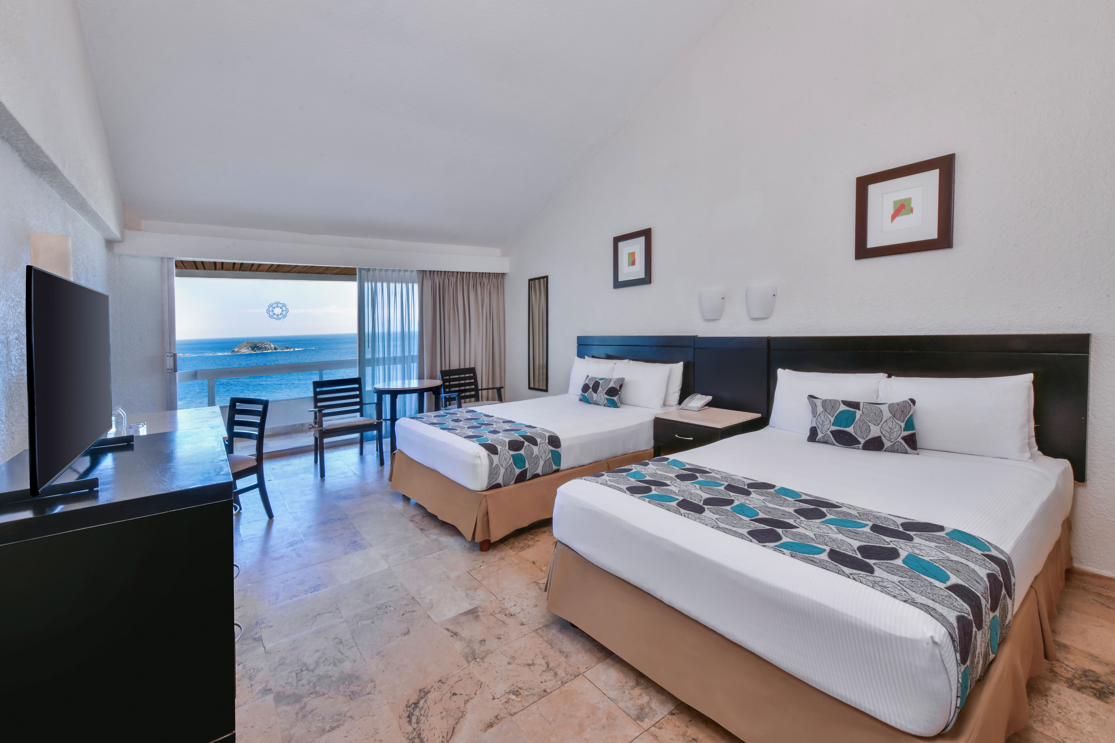 A hotel room with two beds, a desk, and a view of the ocean.