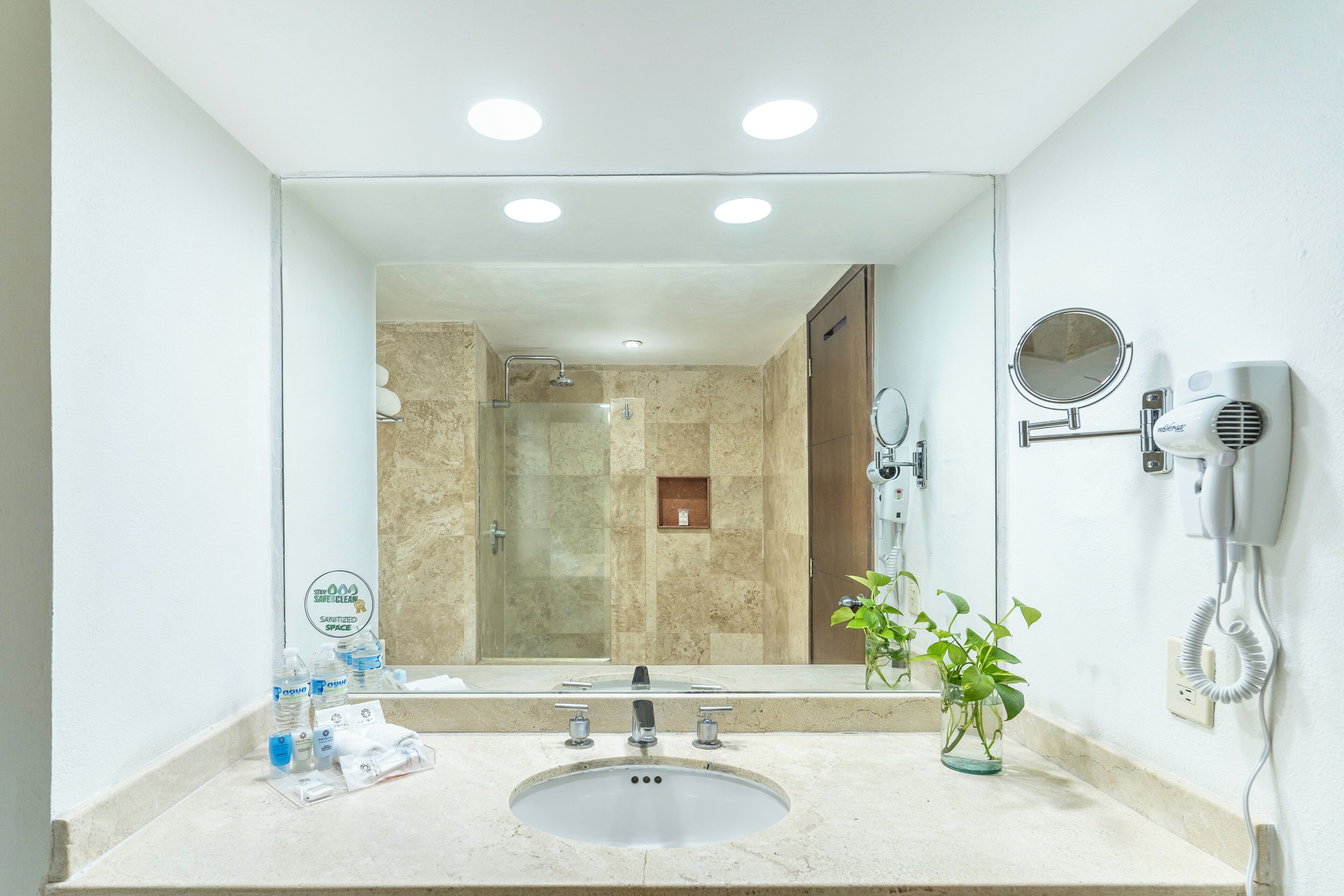 A modern bathroom with a large mirror, a sink, a hairdryer, and a shower area.