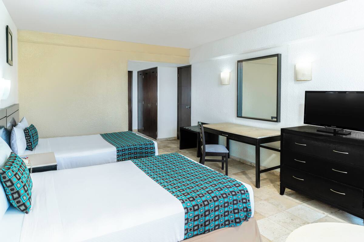 Une chambre d’hôtel avec deux lits, un bureau, une télévision et une commode.