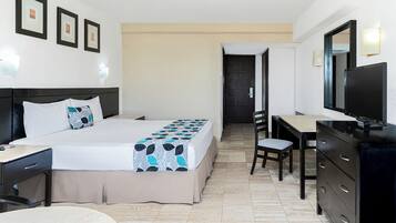 A hotel room with a bed, desk, chair, dresser, and a TV.