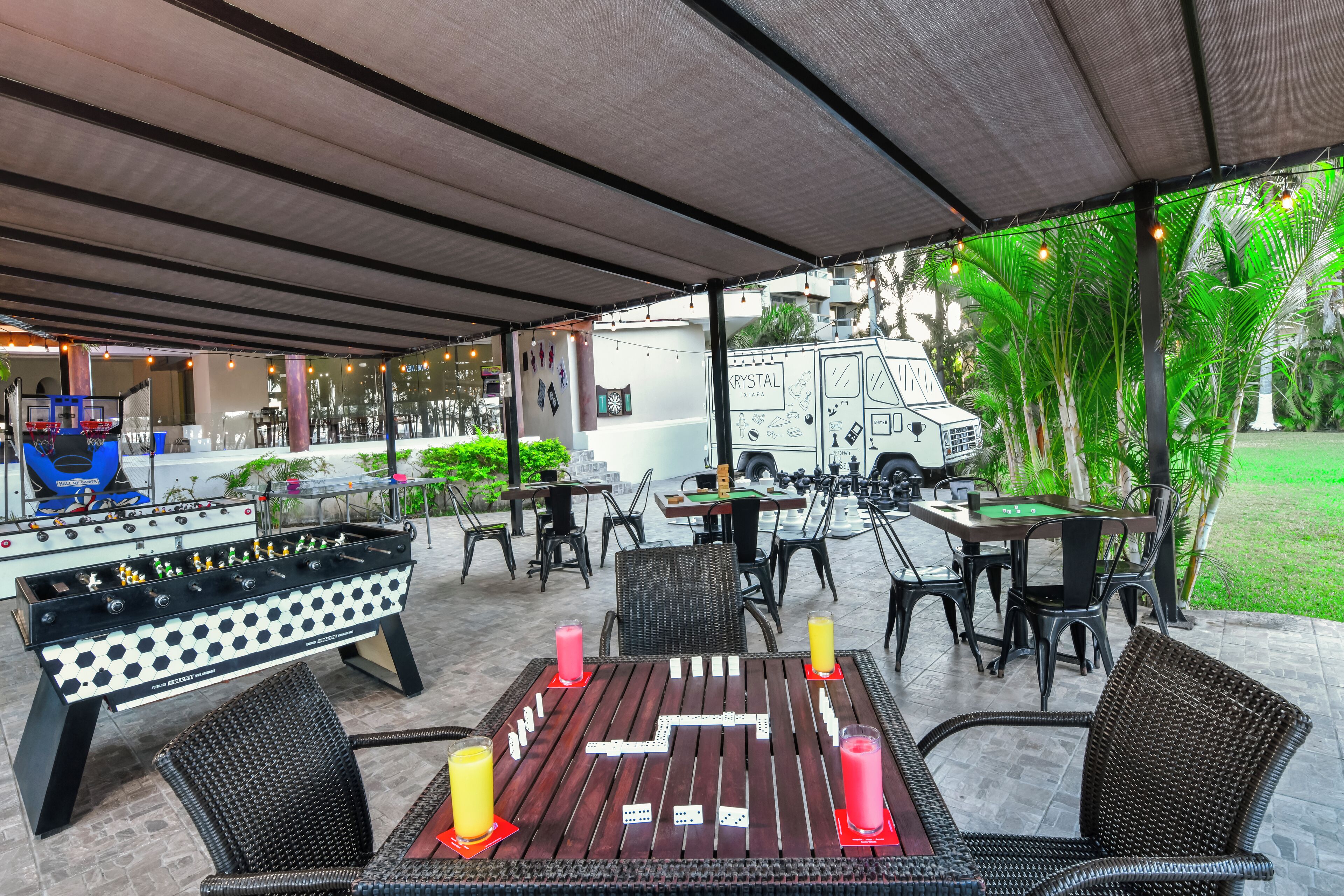 En udendørs patio med et bordtennisbord, spiseborde, stole og en lastbil med teksten 'CRYSTAL RESTAURANT'.