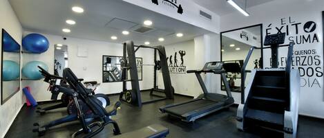 Une salle de sport équipée de tapis de course, d’appareils de musculation et de ballons d’exercice.