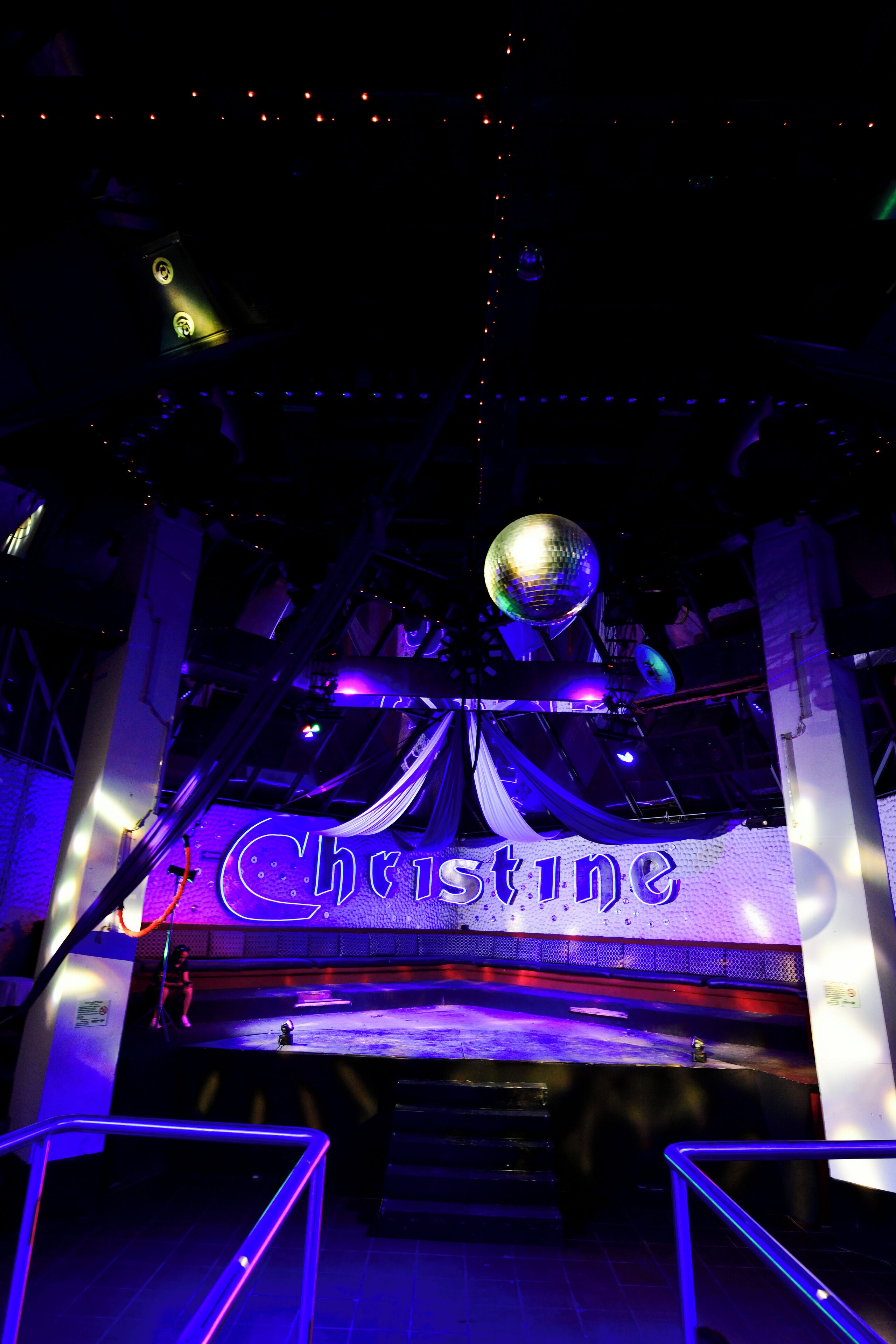 A venue with a prominent 'Christine' sign, a disco ball, and draped fabric.