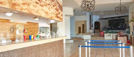 A hotel lobby with a reception desk, a staircase leading to the upper floor, and a seating area.