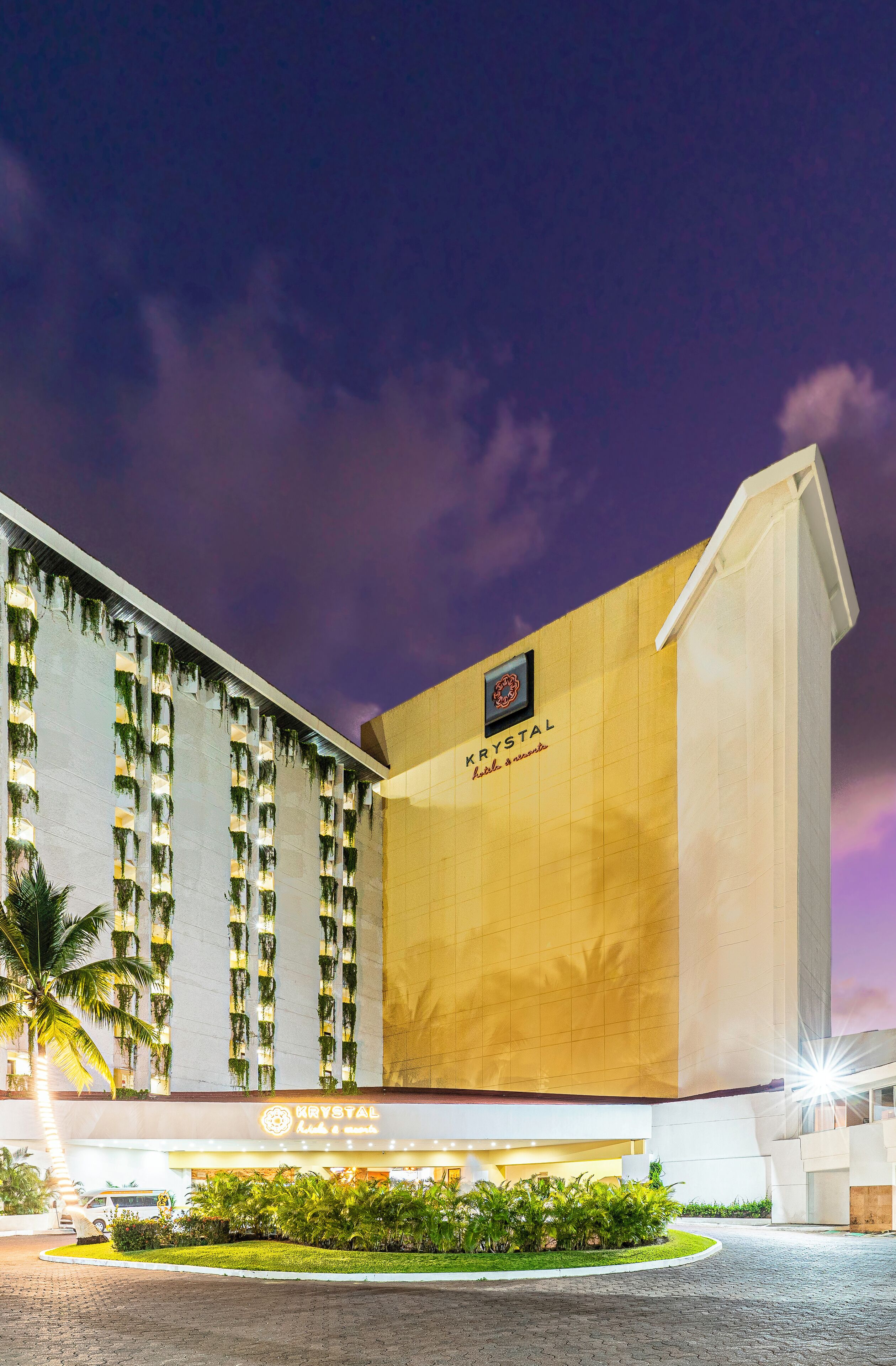 A hotel with a modern facade, a prominent logo, and a well-maintained garden area in front.