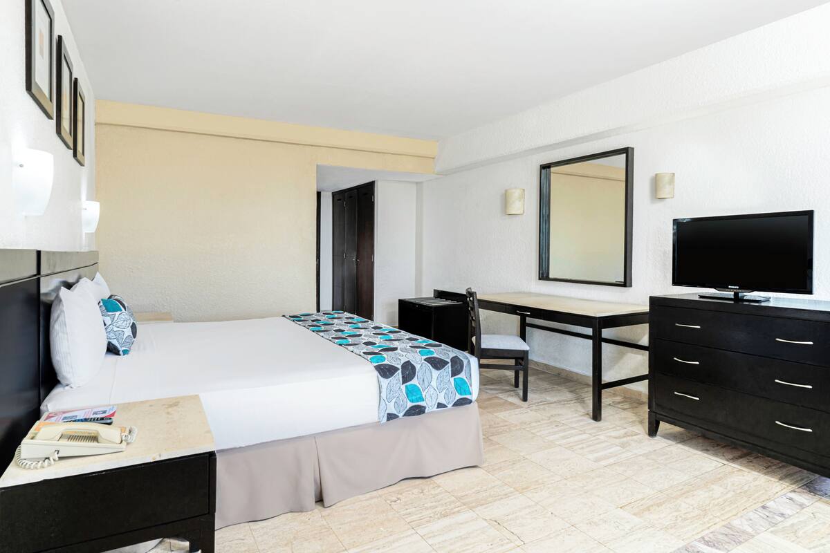 Une chambre d’hôtel équipée d’un lit, d’un bureau, d’une chaise, d’une commode et d’un téléviseur.