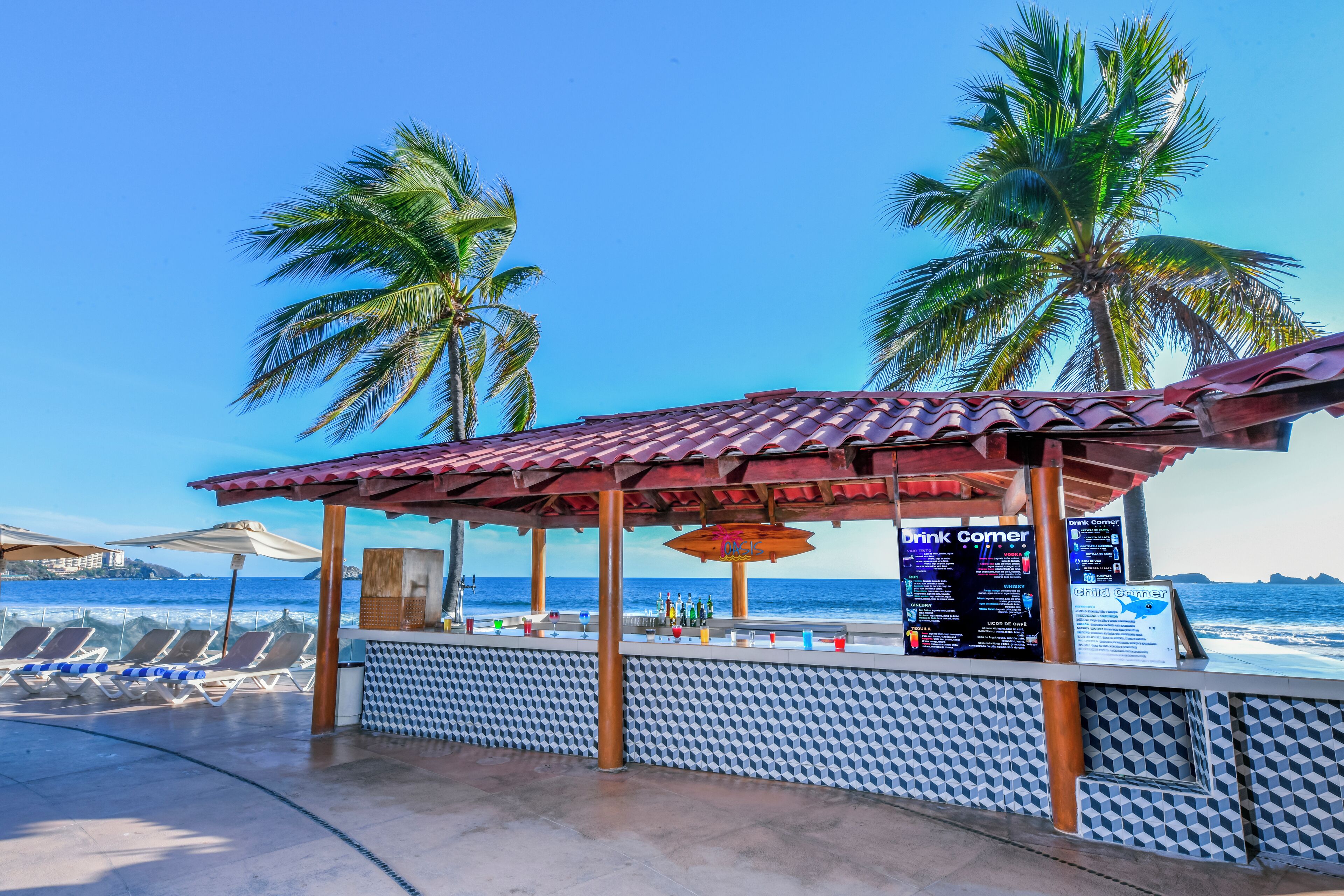 A beachside bar with a tiled roof, palm trees, and a view of the ocean.