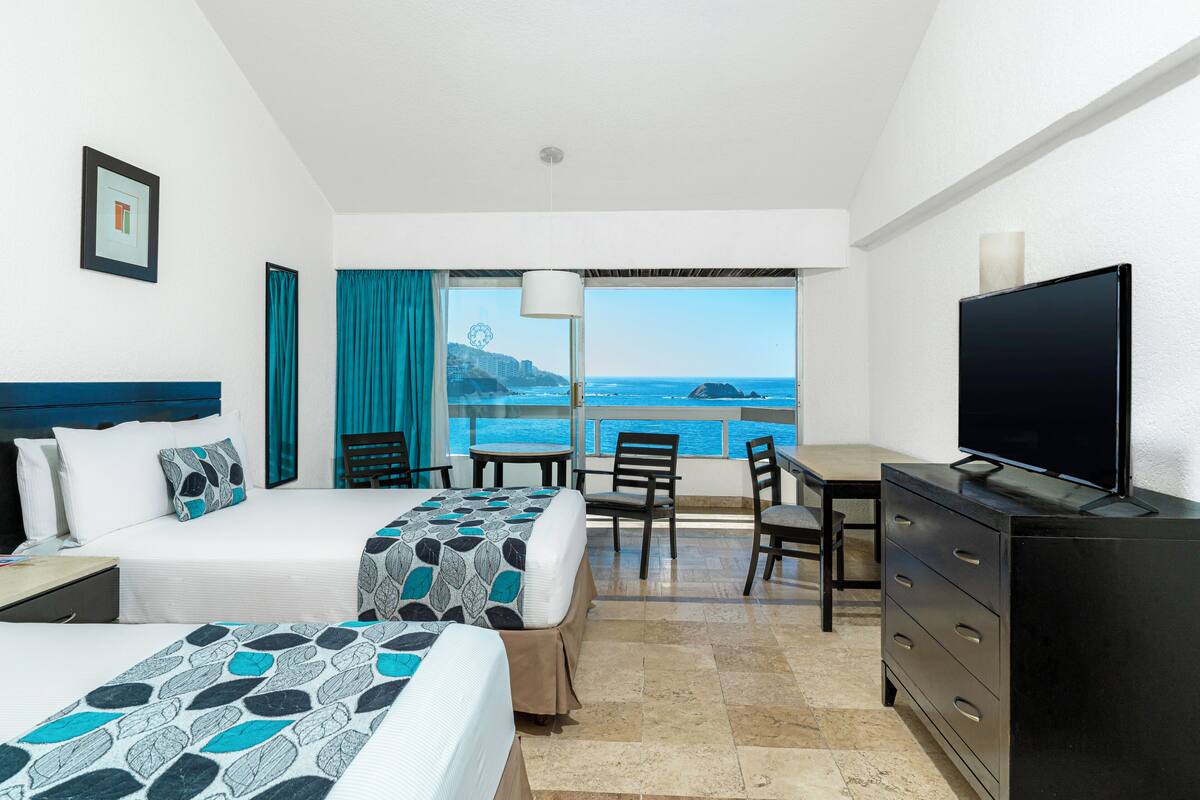 Une chambre d’hôtel avec deux lits, un bureau, une télévision et un balcon donnant sur l’océan.