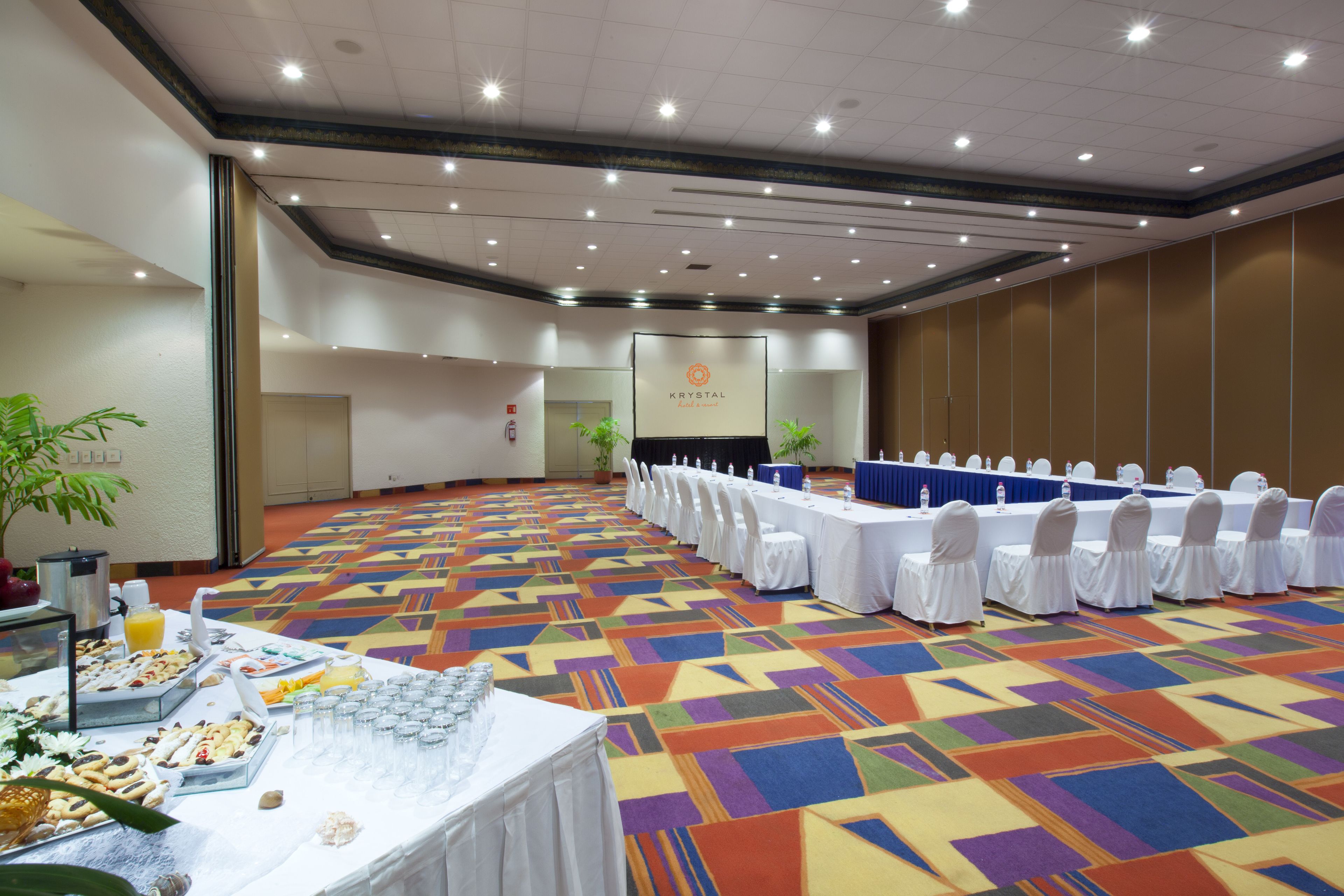A conference room with a long table set for a meeting, a buffet table with food and drinks, and a sign that reads "KRYSTAL".