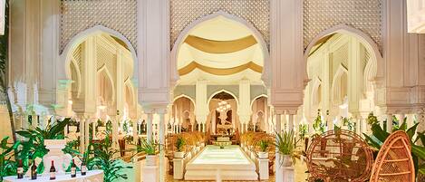 A luxurious lobby with a checkered floor, a central fountain, ornate arches, and wicker furniture.