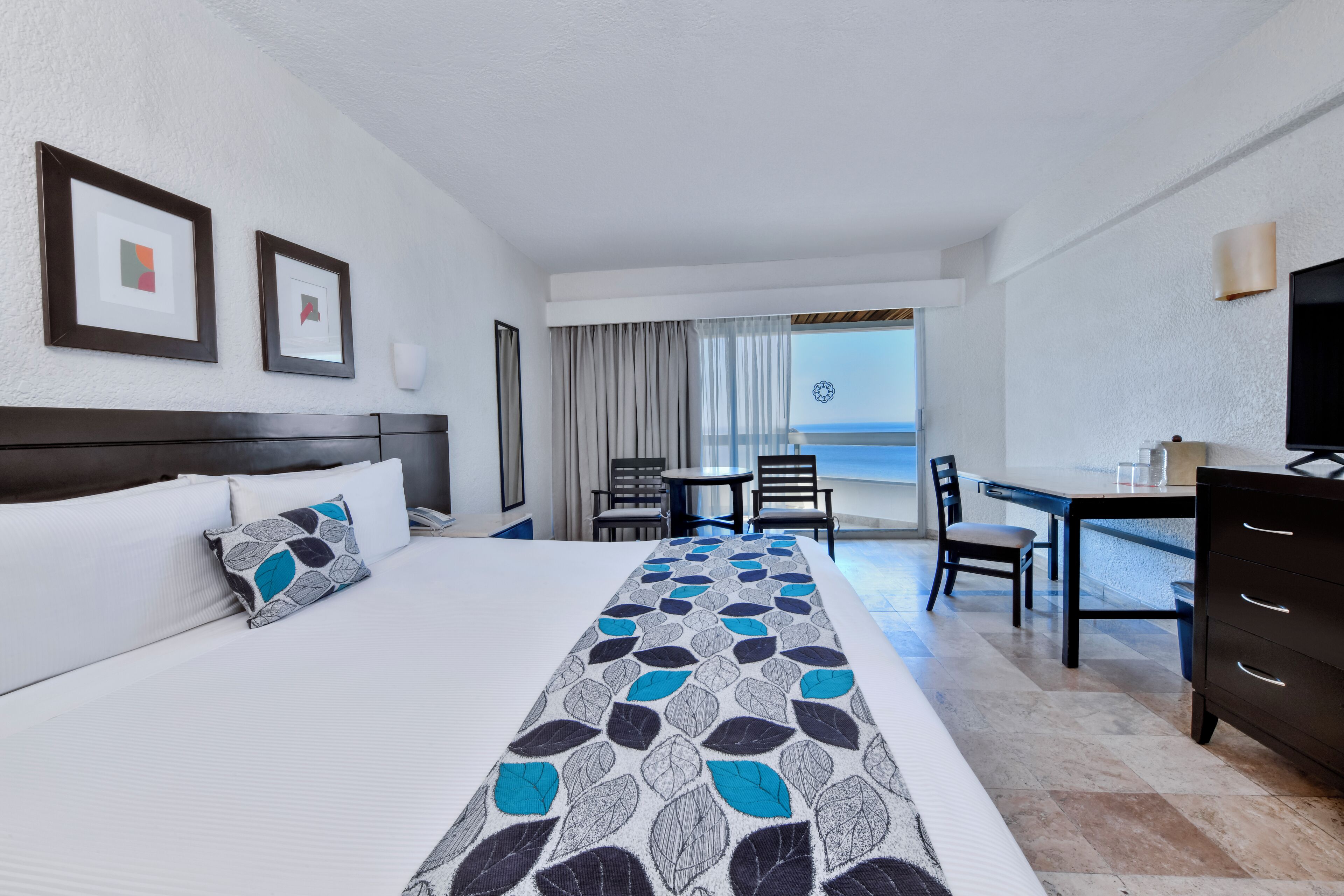 Een hotelkamer met een bed, een bureau, een stoel en uitzicht op het strand.