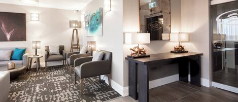 A modern hotel room with a sofa, armchairs, a coffee table, a desk, and a mirror.